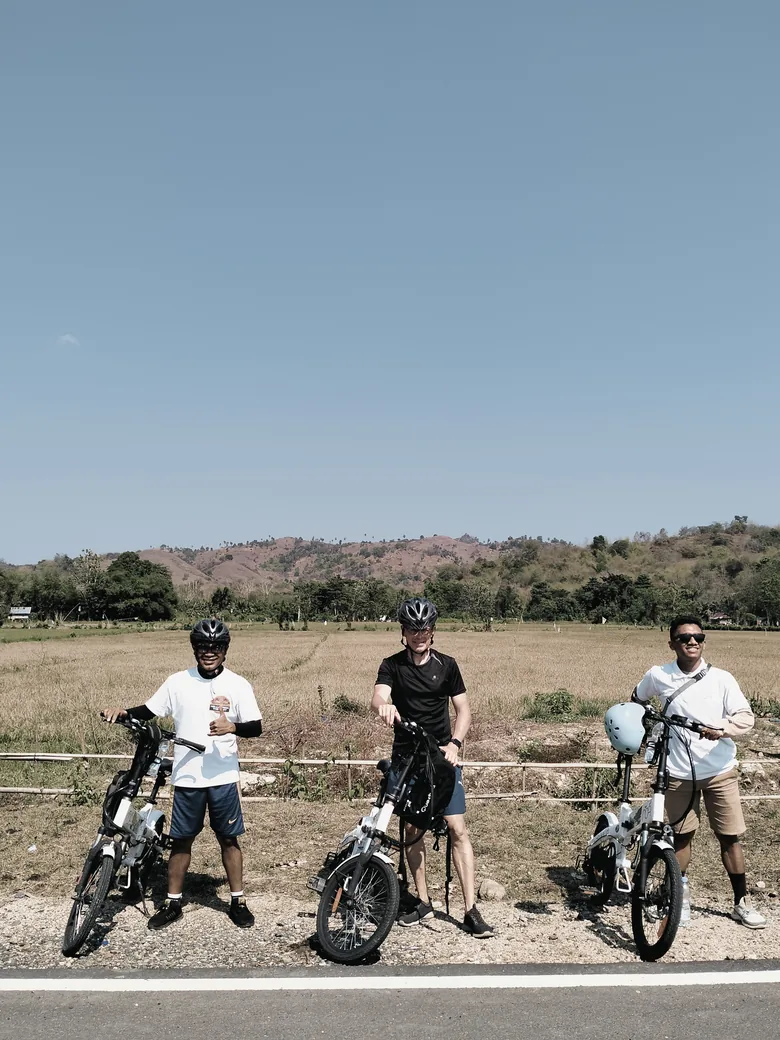 Cyclists pausing beside Bali rice fields and hills during an educational cycling tour