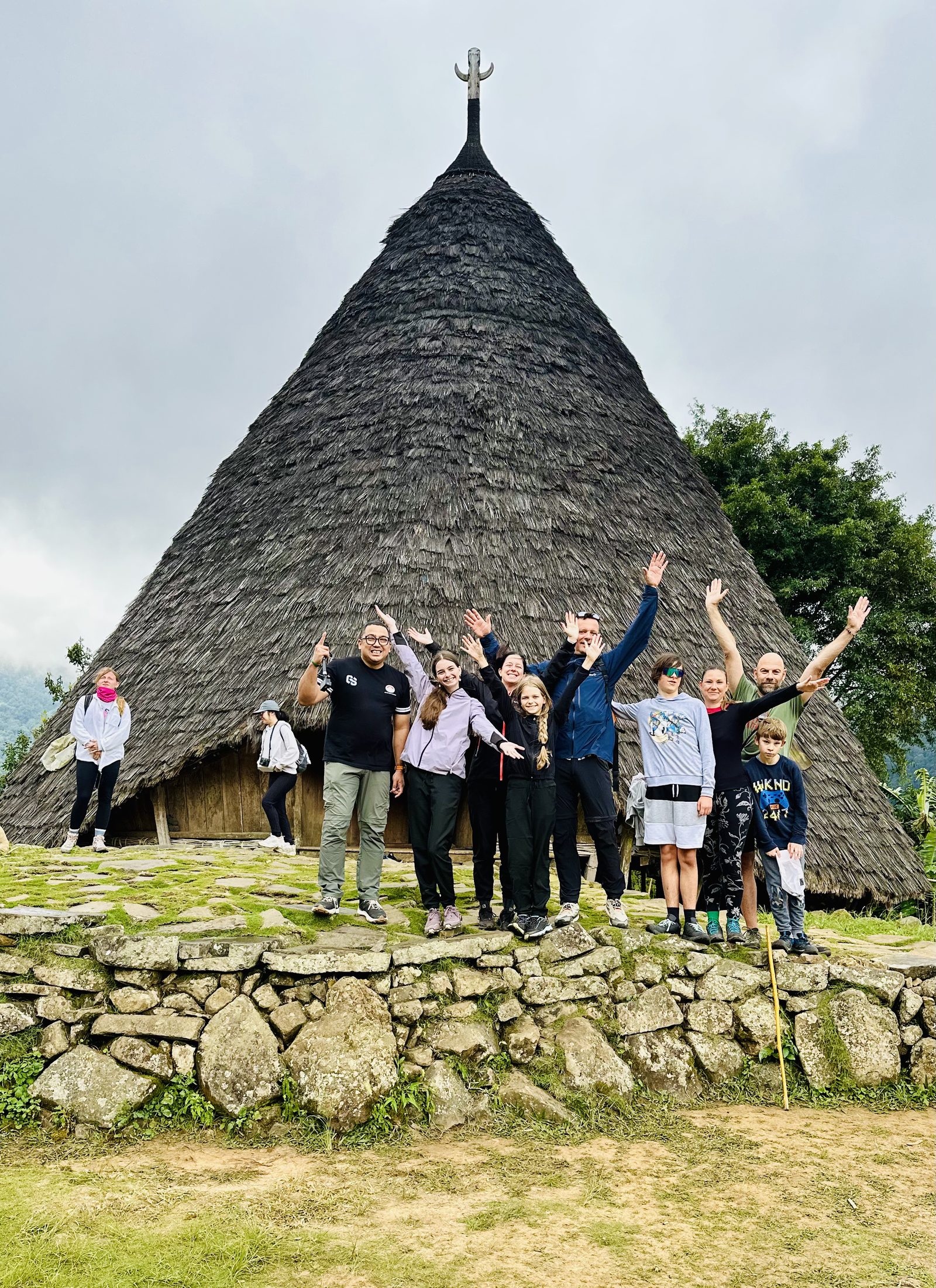 Herdi with a family of guests in front of a Mbaru Niang house at Waerebo village